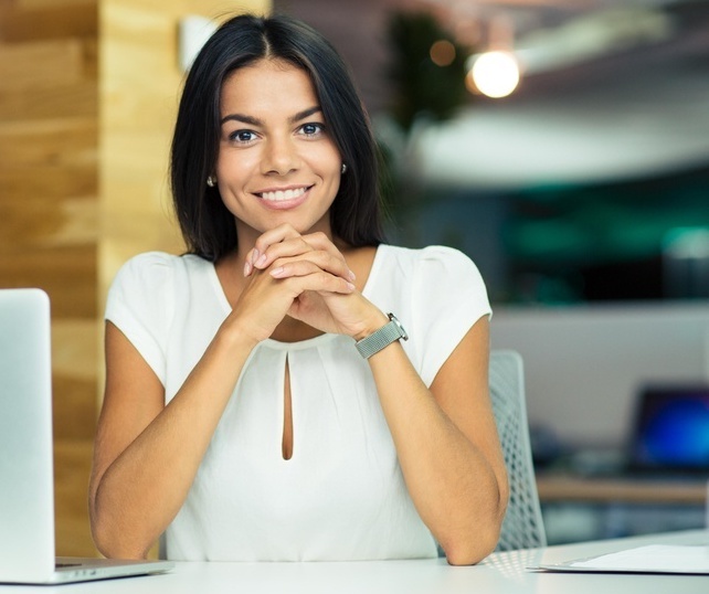 Portrait of a cheerful businesswoman sitting at the table in office and looking at camera