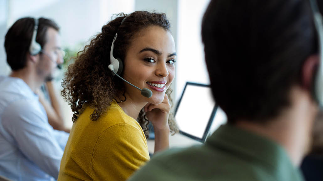 Female customer service worker smiling into the camera sitting between two male colleagues